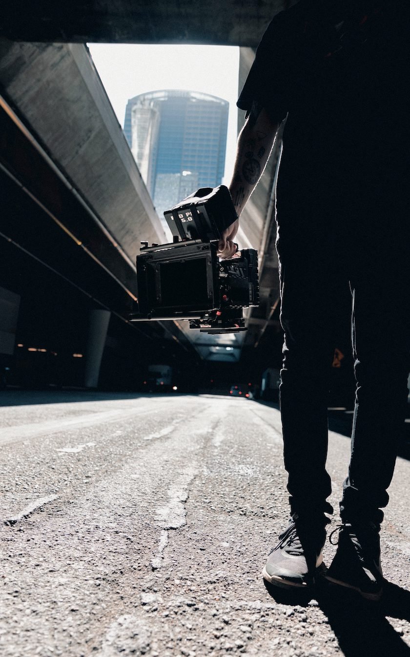 Photograph of a person standing and holding a camera in a city